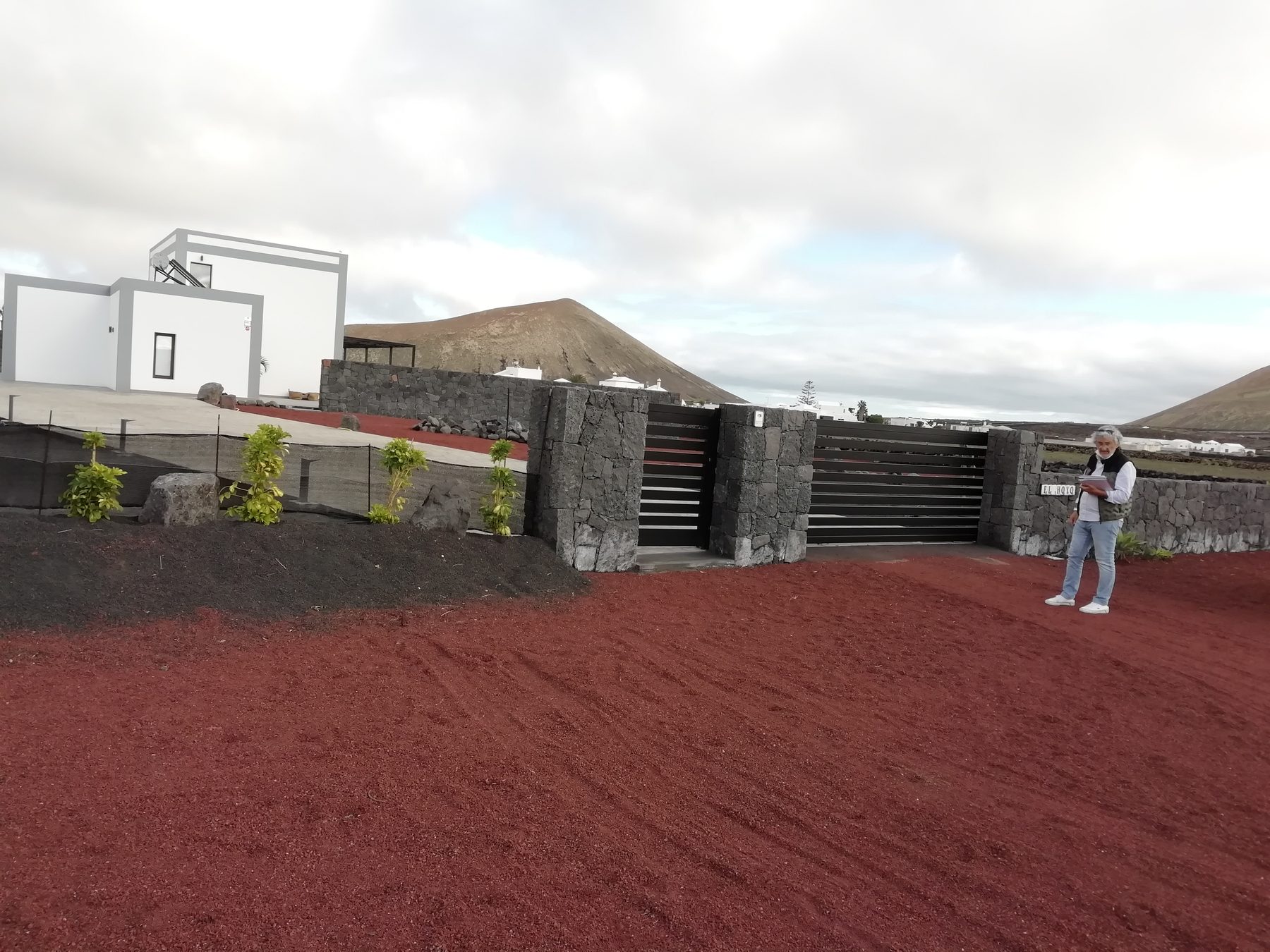 Portón de lamas de aluminio negro entre muros de piedra volcánica